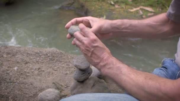 Movimento lento de um homem cuidadosamente selecionando pedras ou rochas ao lado de um rio fluindo — Vídeo de Stock