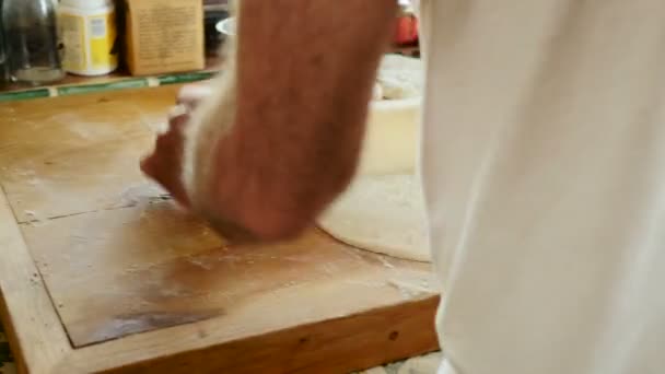 A man uses a rolling pin on a wooden cutting board in his home kitchen — Stock Video