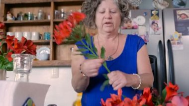 Onun 60s bir kadında taze kesme çiçekler onun mutfakta bir vazoda düzenler