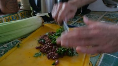 Yaşlı bir adam bir kesme tahtası pişmemiş karaciğer ile taze maydanoz bir bıçakla pirzola.