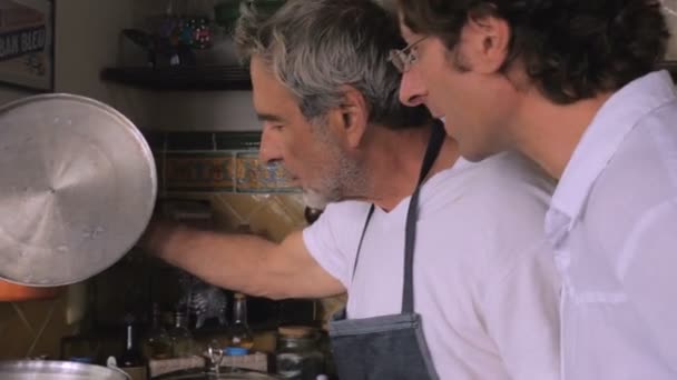 Un padre y un hijo mayores mirando dentro de una olla de comida que están preparando — Vídeo de stock