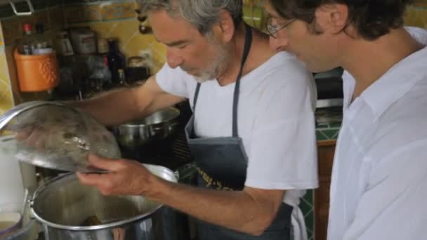 Un homme dans la soixantaine rince la nourriture dans un grand pot tandis qu'un homme d'âge moyen aide — Video