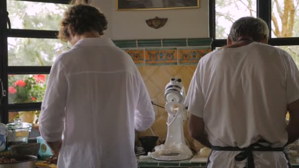 Двоє чоловіків готують їжу на кухні, знятій ззаду у повільному русі — стокове відео