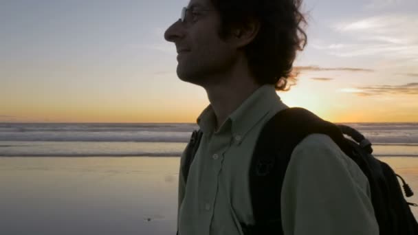 Рука тримається за мандрівника, що йде вздовж пляжу під час заходу сонця з рюкзаком — стокове відео