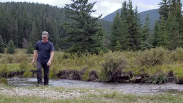 Un hombre con una caña de pescar pasa frente a la cámara lejos de un río — Vídeo de stock