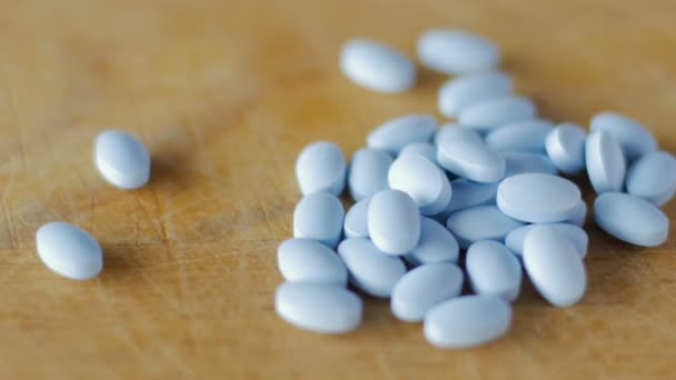 Close up de pílulas azuis girando em uma placa de madeira — Vídeo de Stock