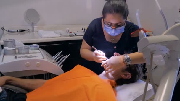 Uma mulher mexicana dentista limpa os dentes de um homem de meia idade — Vídeo de Stock