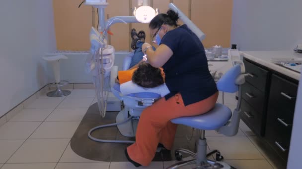 A Mexican dentist works on a dental patient - wide dolly from behind — Stock Video