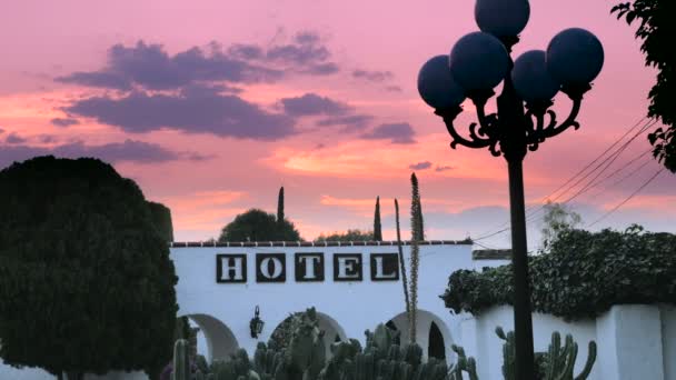 Un cartel del hotel en una pared blanca arqueada contra una dramática puesta de sol — Vídeos de Stock