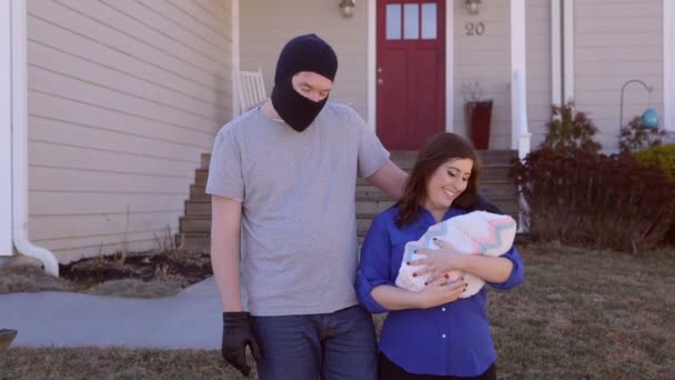 En man klädd i en ski mask har sin arm kring en kvinna med en baby — Stockvideo