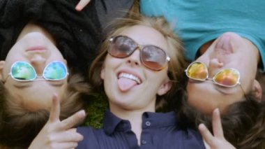 Çimlerin içinde yatan üç genç kız kameraya aptal suratlar yapıyor.