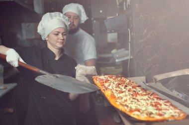 Şef baker aşçı pizza lokanta mutfağı kürek ile fırın içine koyarak siyah üniformalı
