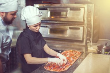 Şef baker aşçı pizza lokanta mutfağı kürek ile fırın içine koyarak siyah üniformalı