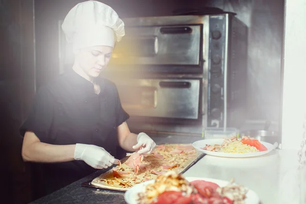 Kocken baker cook i svart uniform sätta pizza i ugnen med spade på restaurang kitchen — Stockfoto