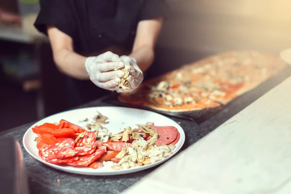 Kocken baker cook i svart uniform sätta pizza i ugnen med spade på restaurang kitchen — Stockfoto