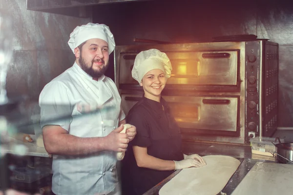 Повар-пекарь в черной форме кладет пиццу в духовку с лопатой на кухне ресторана — стоковое фото