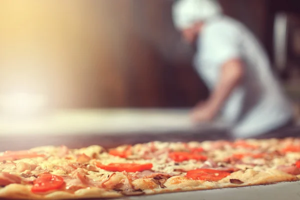 Chef panadero cocinero en uniforme negro poner pizza en el horno con pala en la cocina del restaurante —  Fotos de Stock