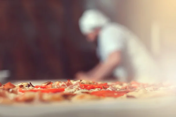 Chef panadero cocinero en uniforme negro poner pizza en el horno con pala en la cocina del restaurante —  Fotos de Stock