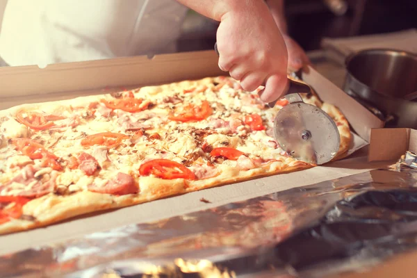 Detailní ruka kuchaře pekaře v bílé uniformě řezání pizzy v kuchyni — Stock fotografie