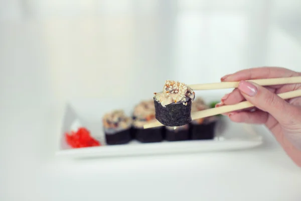 Primo piano di bacchette prendendo porzione di rotolo di sushi sul tavolo ristorante / mangiare rotolo di sushi con le bacchette — Foto Stock