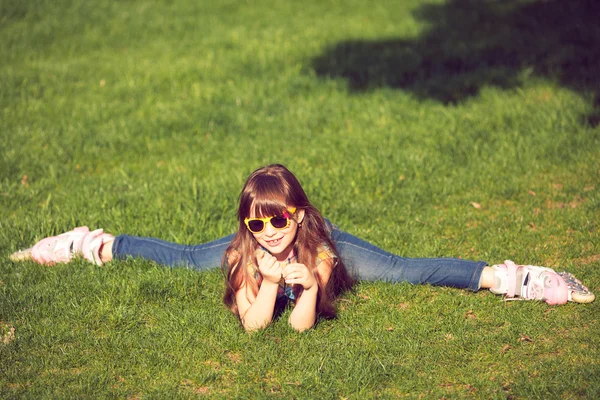 Menina vestindo patins sentados na grama no parque — Fotografia de Stock