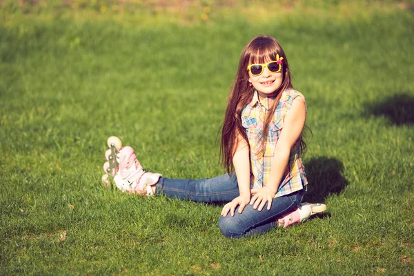 Flickan bär rullskridskor sitter på gräset i parken — Stockfoto