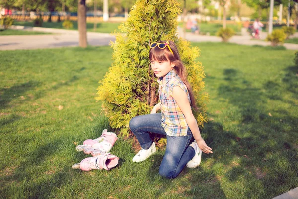 Flickan bär rullskridskor sitter på gräset i parken — Stockfoto