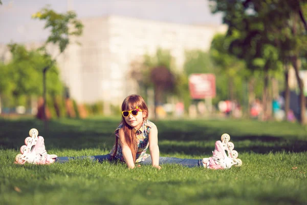 Дівчина в роликових ковзанах сидить на траві в парку . — стокове фото