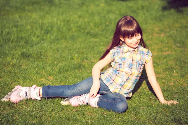 公園の芝生の上に座ってのローラー スケート靴を着ている少女. — ストック写真