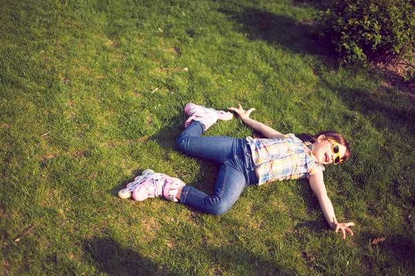 Flickan bär rullskridskor sitter på gräset i parken. — Stockfoto