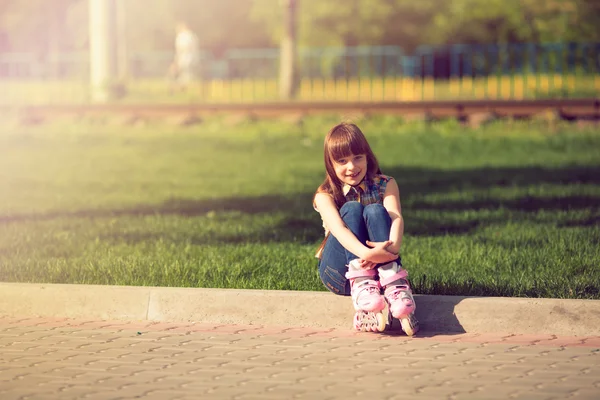 Mädchen mit Rollschuhen sitzt auf Gras im Park. — Stockfoto