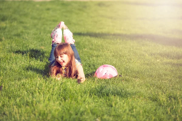 Menina vestindo patins sentados na grama no parque . — Fotografia de Stock