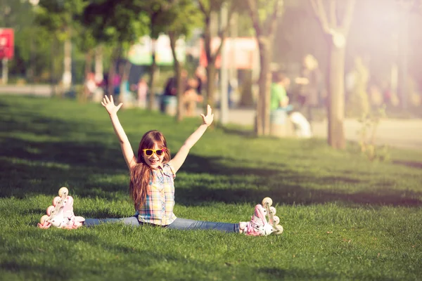 Fille portant des patins à roulettes assis sur l'herbe dans le parc . — Photo