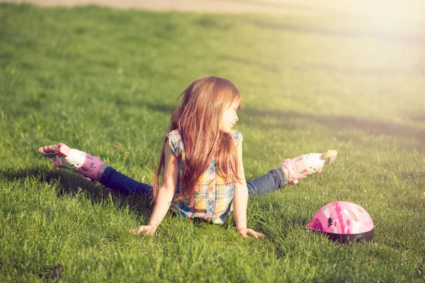 Flickan bär rullskridskor sitter på gräset i parken. — Stockfoto