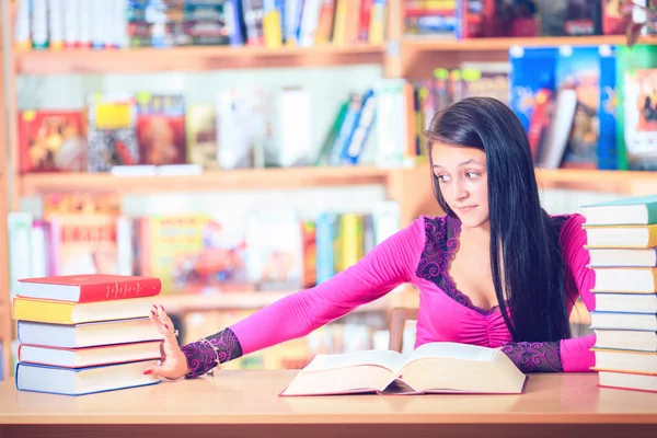 Estudante com óculos lendo livros na biblioteca — Fotografia de Stock