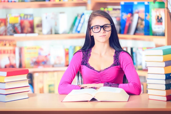 Estudante com óculos lendo livros na biblioteca — Fotografia de Stock