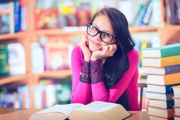 Девушка в очках читает книги в библиотеке — стоковое фото