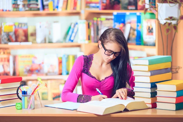 Estudante com óculos lendo livros na biblioteca — Fotografia de Stock