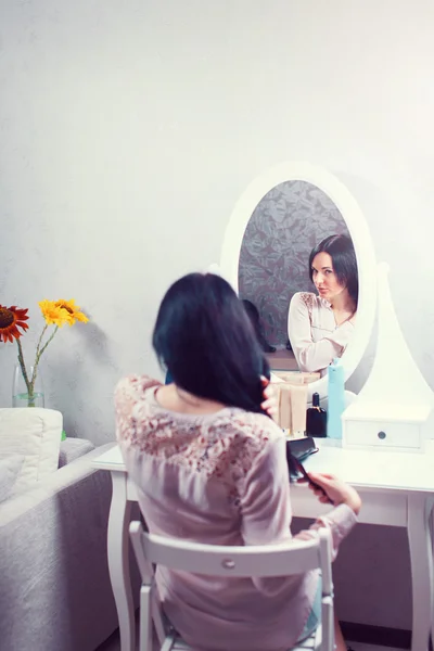 Retrato de uma mulher bonita como aplicação de maquiagem perto de um espelho . — Fotografia de Stock