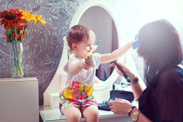 Mother and daughter sitting at dressing table at house.