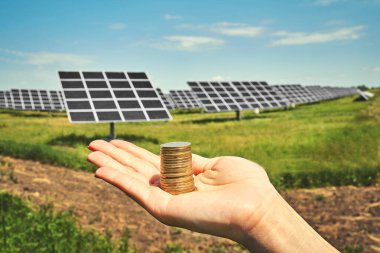 Arka planda fotovoltaik güneş enerjisi panelleri olan el ele tutuşma para banknotu, 