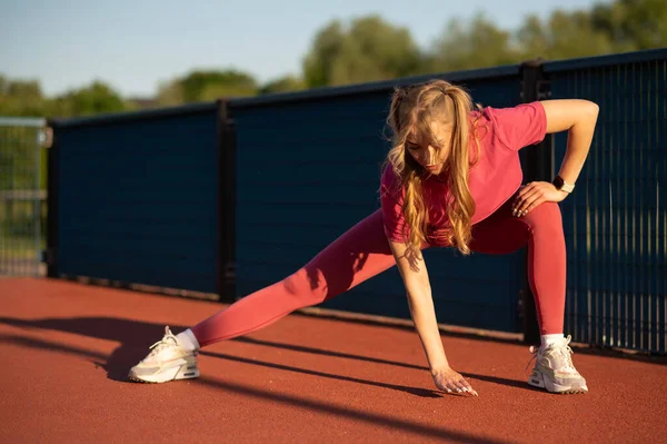 Atletik giyinen sarışın kadın, güneşli bir sonbahar gününde açık havada esniyor..