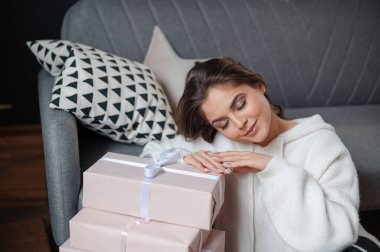 Hediye kutularıyla kanepede oturan ve gülümseyen rahat kazaklı kadın..