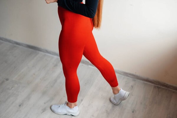 Человек в красных леггинсах и белых кроссовках на деревянном полу.