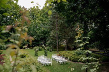 Beyaz sandalyeler ve yemyeşil bahçedeki çiçek kavisli açık hava düğün töreni..