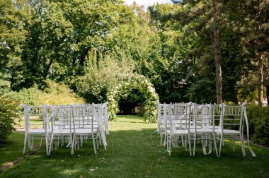 Beyaz sandalyeler ve çiçek kemerleriyle kurulmuş açık hava düğün töreni..