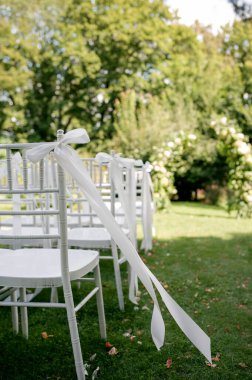 Beyaz sandalyeler ve kurdelelerle kurulmuş açık hava düğün töreni..