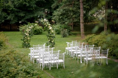Beyaz sandalyeler ve çiçek kemerleriyle kurulmuş açık hava düğün töreni..