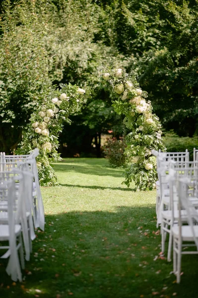 Çiçekli kemer ve beyaz sandalyeli açık hava düğün töreni..
