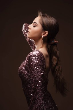 Parlak elbiseli zarif bir kadın. Gözleri kapalı ve zarif duruşuyla poz veriyor. Moda fotoshoot stüdyoda.